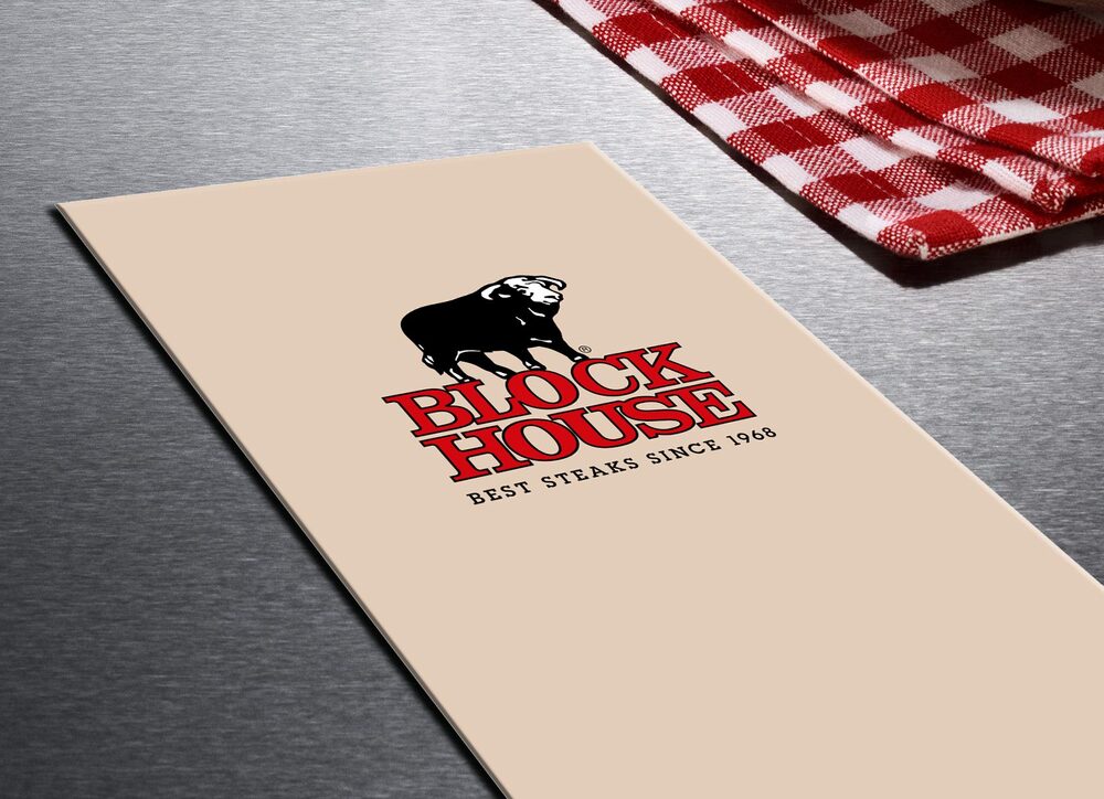 BLOCK HOUSE Speisekarte liegt auf einem grauen Tisch. Rechts oben in der Ecke ist die rot-weiß karrierte Tischdecke zu sehen. 