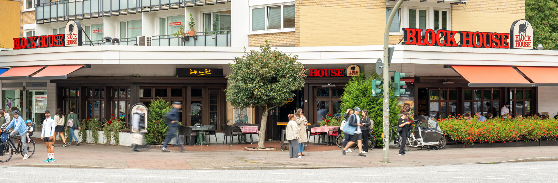 Außenansicht des BLOCK HOUSE Hamburg-Eppendorf mit Terrasse und Passanten an der Straße.