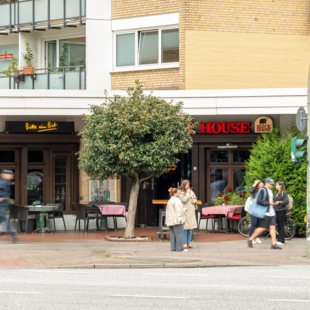 Außenansicht des BLOCK HOUSE Hamburg-Eppendorf mit Terrasse und Passanten an der Straße.
