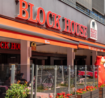 Außenansicht des BLOCK HOUSE Berlin Am Alexanderplatz mit Terrasse, Gästen an Tischen und Blick auf die Straße nahe dem Neptunbrunnen