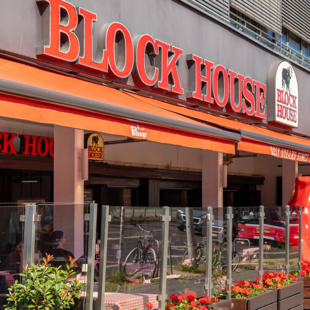 Außenansicht des BLOCK HOUSE Berlin Am Alexanderplatz mit Terrasse, Gästen an Tischen und Blick auf die Straße nahe dem Neptunbrunnen