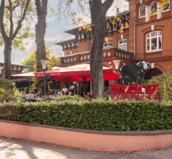 BLOCK HOUSE Hamburg Othmarschen mit Terrasse, roten Sonnenschirmen und Gästen vor dem Steakhouse im grünen Umfeld