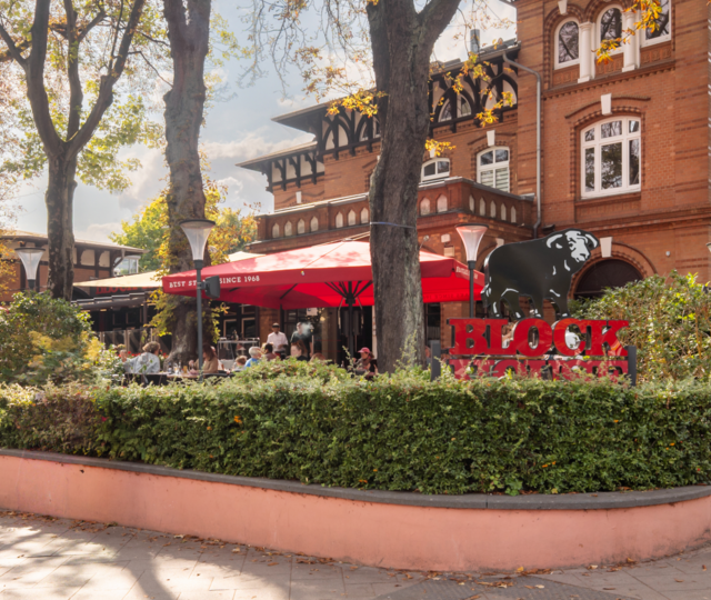 BLOCK HOUSE Hamburg Othmarschen mit Terrasse, roten Sonnenschirmen und Gästen vor dem Steakhouse im grünen Umfeld