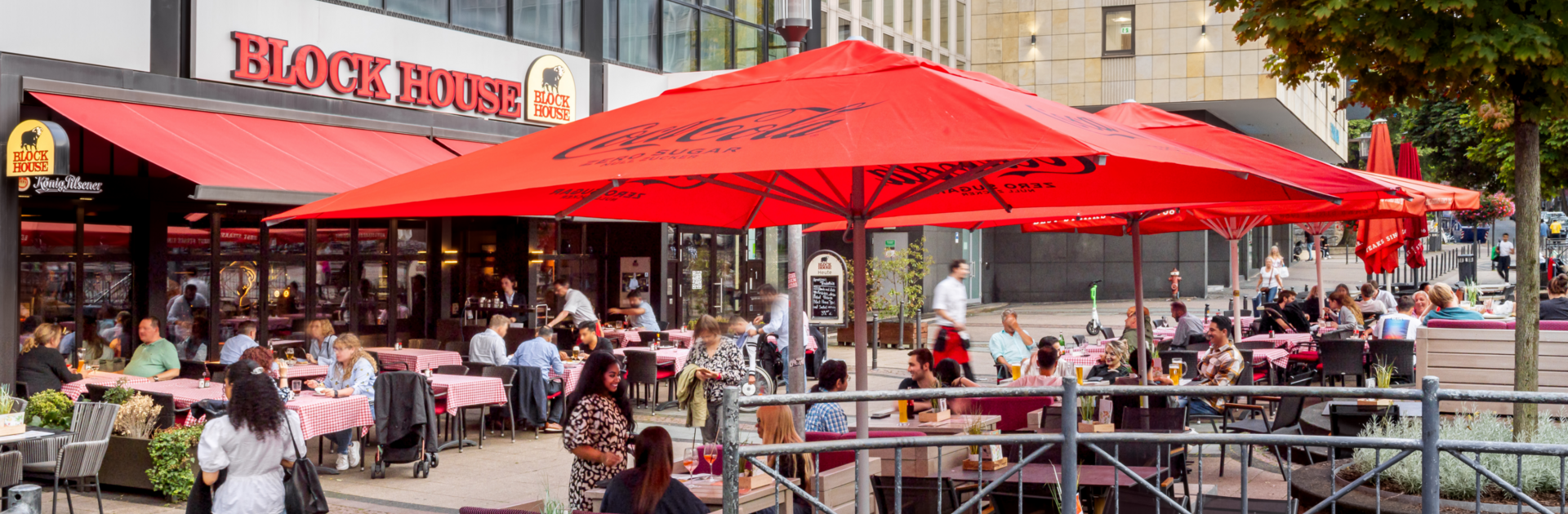 Außenansicht des BLOCK HOUSE Essen mit großer Terrasse, roten Sonnenschirmen und Gästen im Außenbereich.