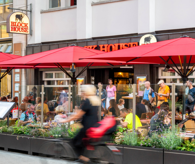 Terrasse des BLOCK HOUSE Hannover Am Kröpcke mit Gästen unter roten Sonnenschirmen in der Fußgängerzone der Innenstadt