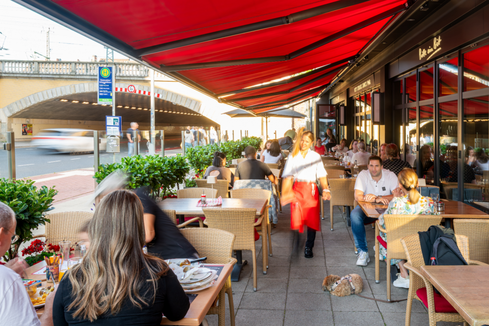 Terrasse des BLOCK HOUSE Hannover am Thielenplatz mit Gästen unter roten Markisen.