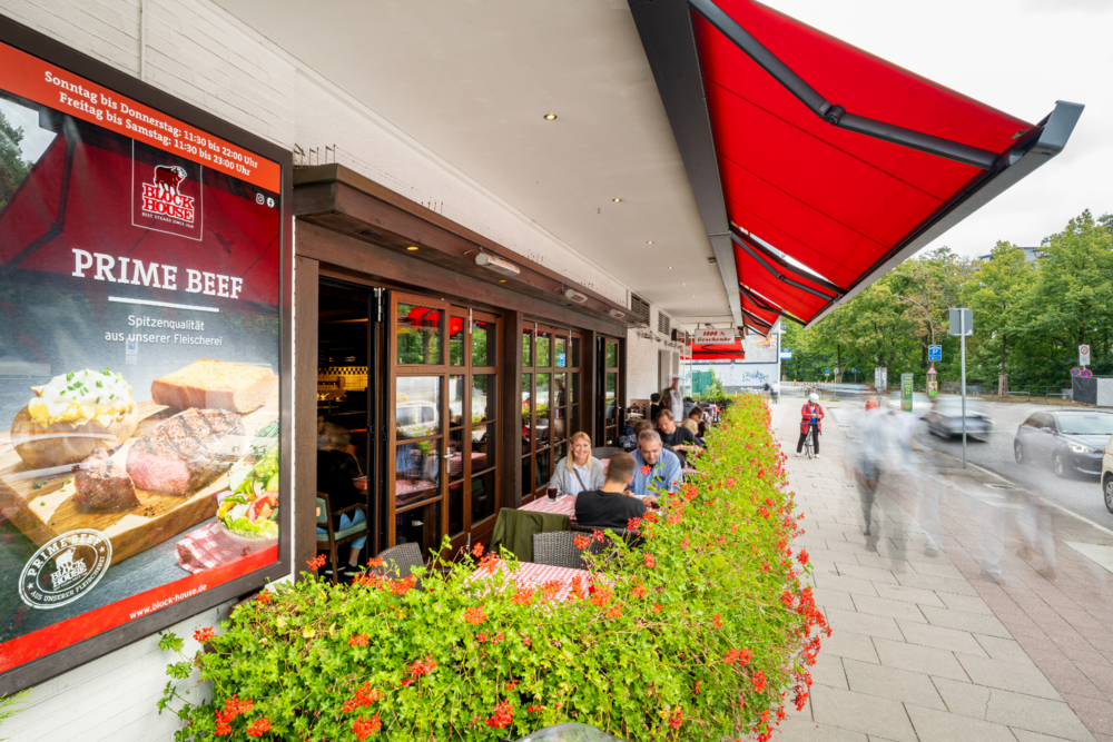 Terrasse des BLOCK HOUSE Hamburg-Eppendorf mit roten Markisen und Gästen im Außenbereich.
