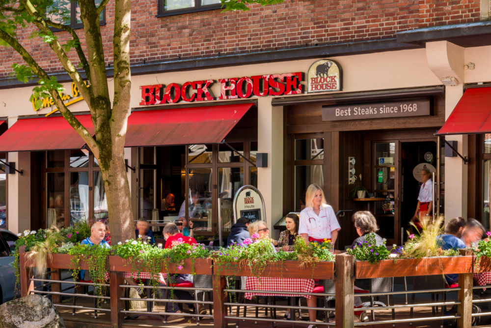 Terrasse des BLOCK HOUSE Kiel mit Gästen, Servicepersonal und begrüntem Außenbereich vor dem Restaurant.