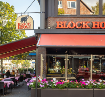 Außenansicht des BLOCK HOUSE Hamburg Barmbek mit Terrasse, roten Markisen und Sitzplätzen vor dem Steakhouse