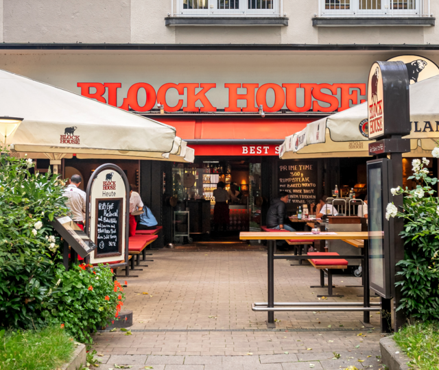Eingang und Terrasse des BLOCK HOUSE München Leopoldstraße mit Sonnenschirmen und Gästen vor dem Steakhouse