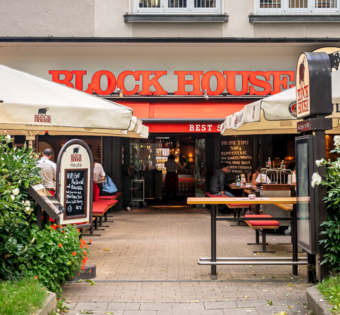 Eingang und Terrasse des BLOCK HOUSE München Leopoldstraße mit Sonnenschirmen und Gästen vor dem Steakhouse